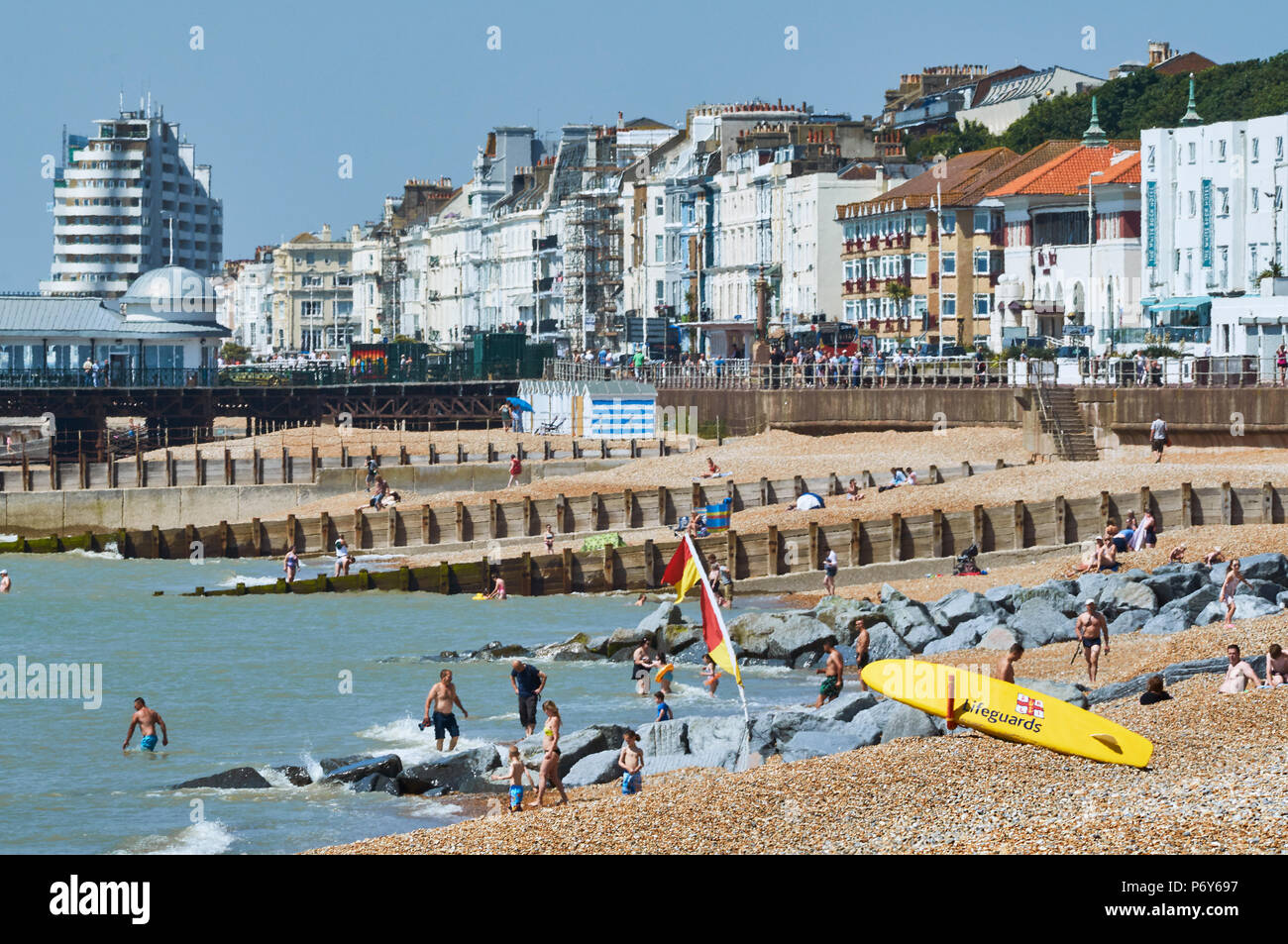 Sunbathers and swimmers on a hot day in June on Hastings Beach, East Sussex, UK, with seafront buildings and Marine Court in background Stock Photo