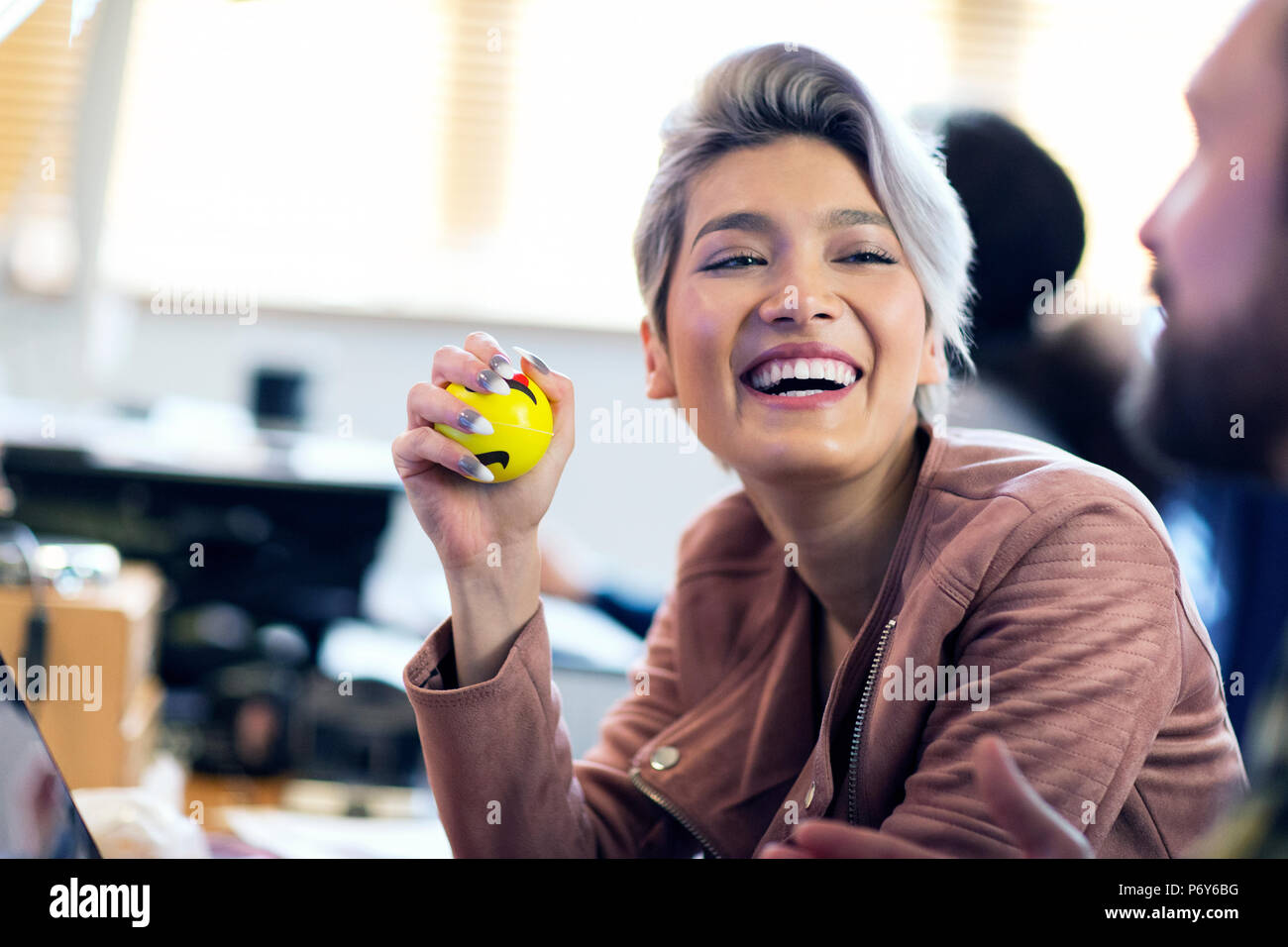 Laughing creative businesswoman squeezing stress ball in office Stock Photo