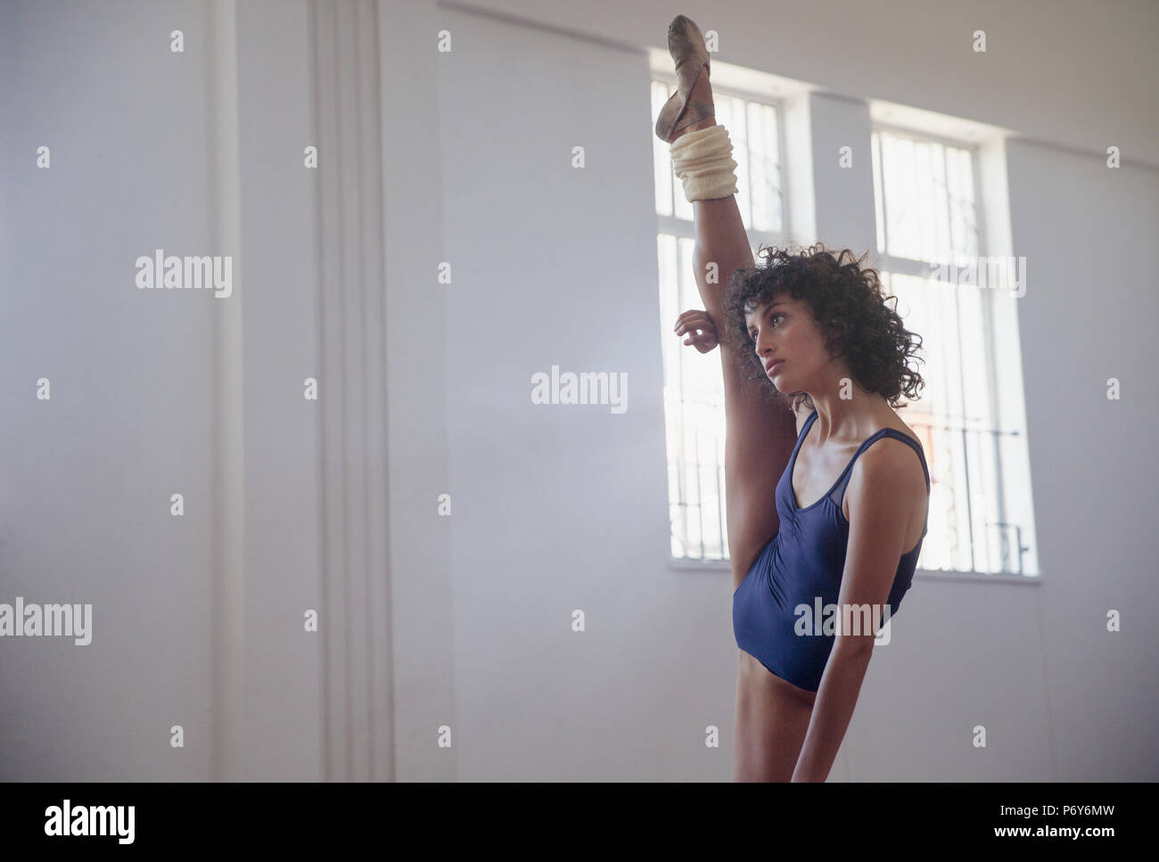 Flexible young female dancer stretching leg, doing standing splits in dance studio Stock Photo