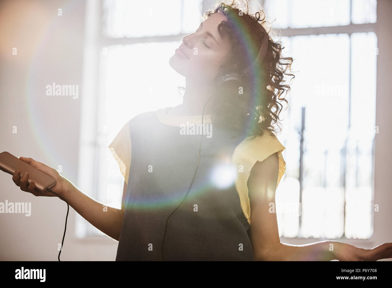 Carefree young female dancer listening to music with headphones and mp3 player in sunny studio Stock Photo
