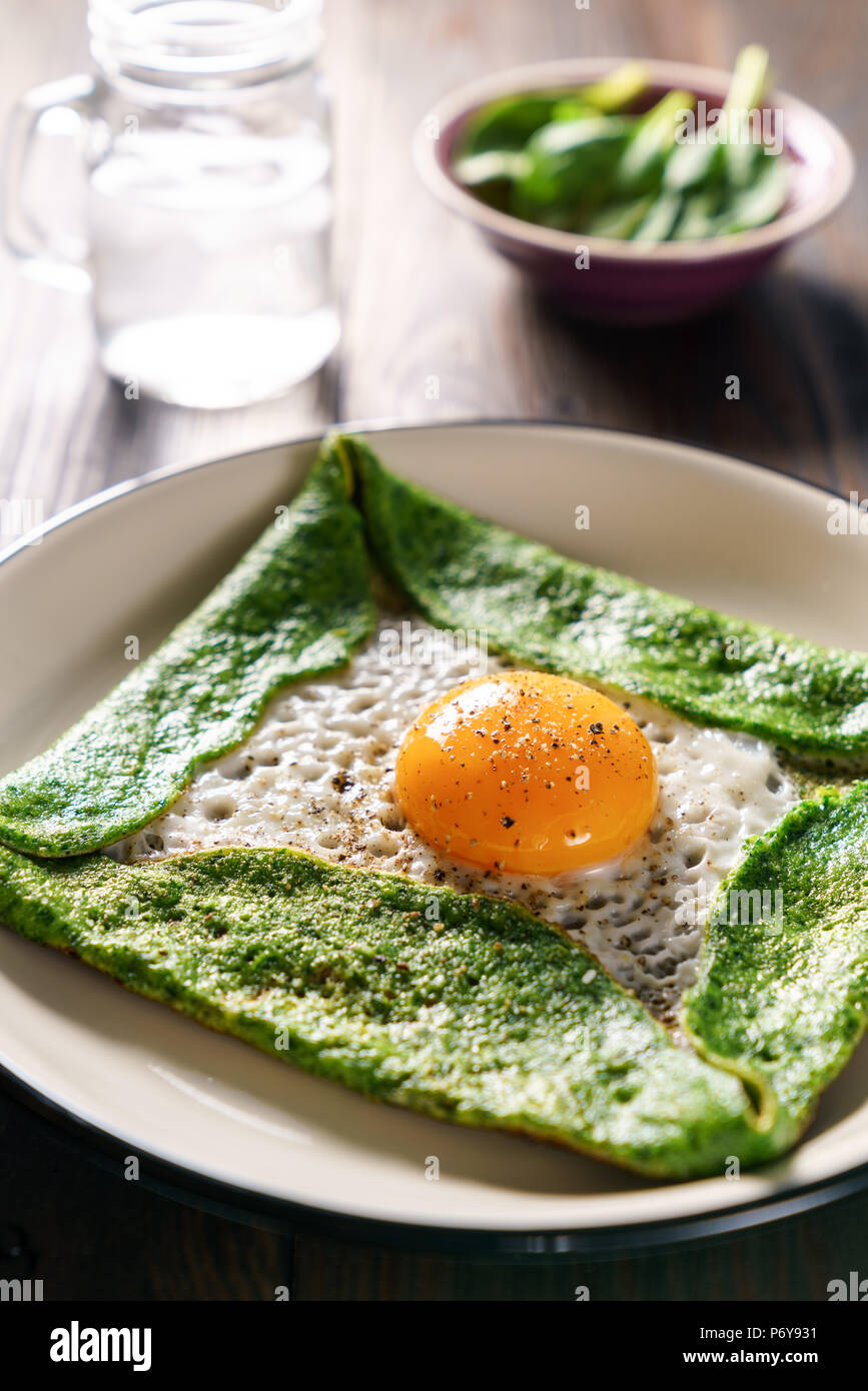 Gluten free spinach crepe with fresh egg on a wooden background Stock Photo