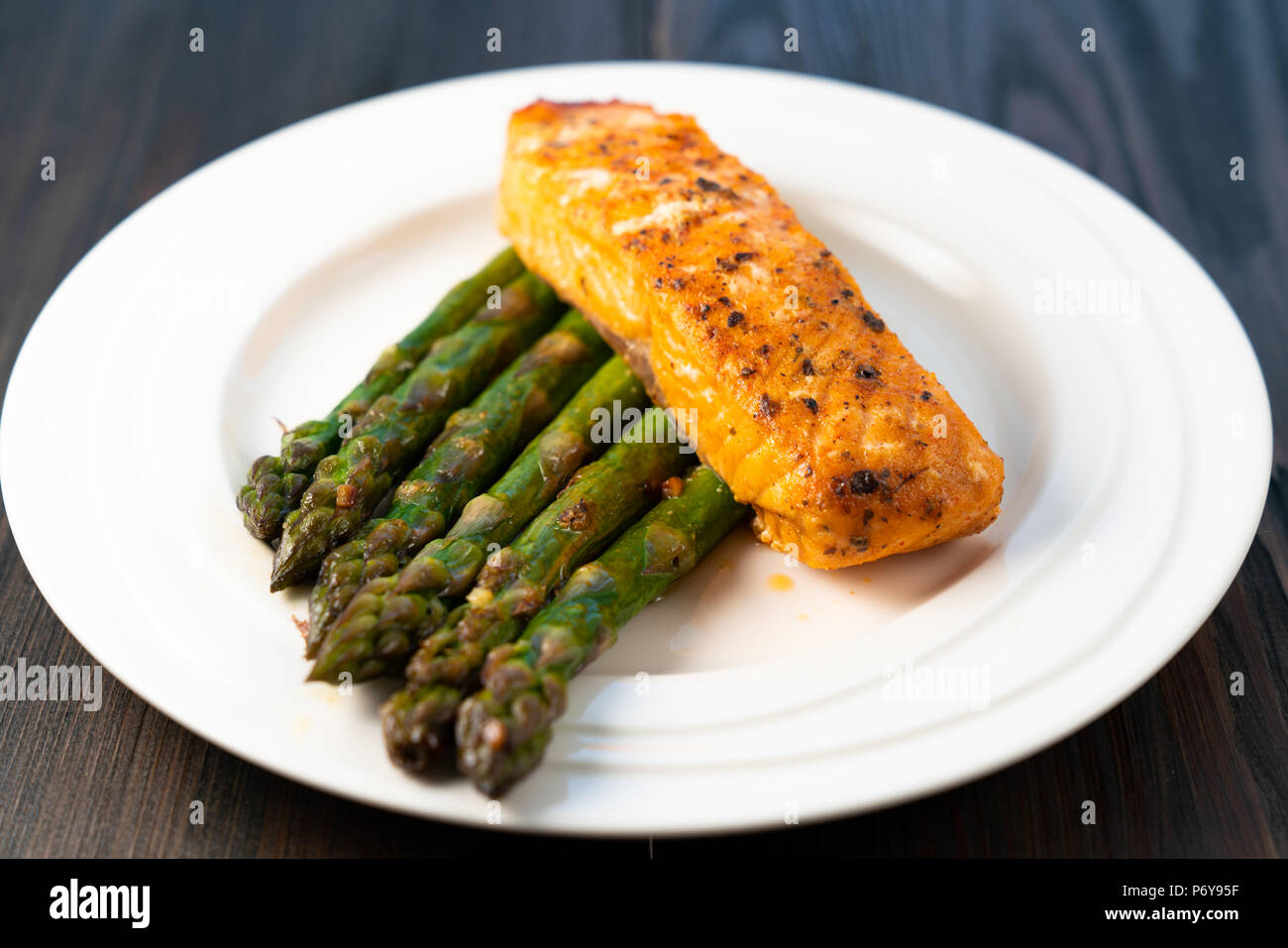 White plate with roasted salmon filet with fried asparagus on a dark wooden background Stock Photo