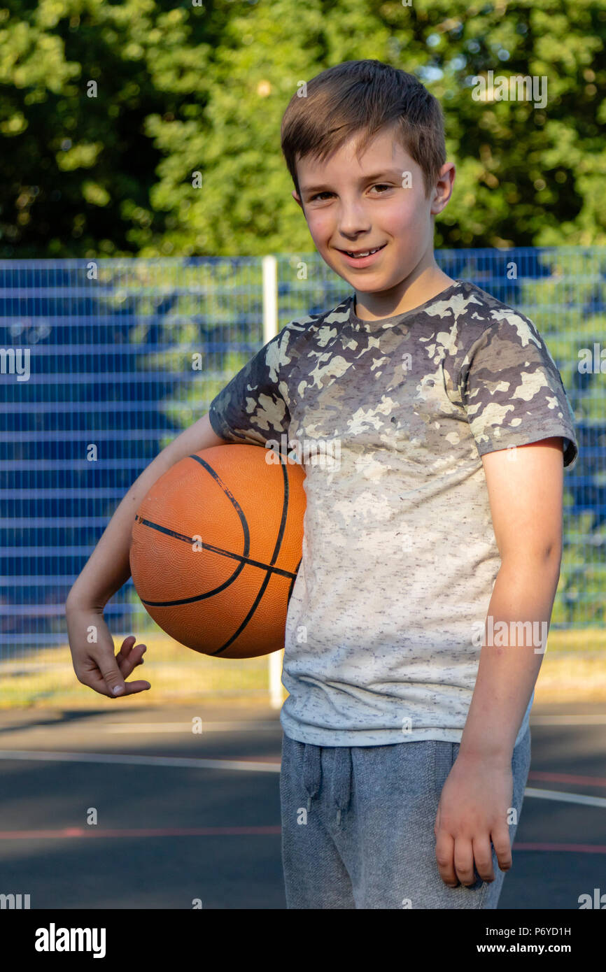 Pre-teen boy holding a basketball on a court in a park Stock Photo