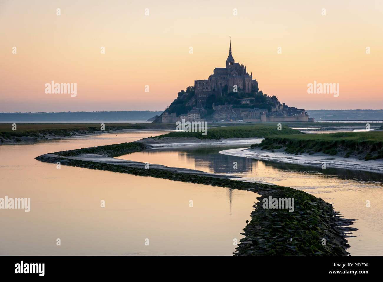 The Mont Saint-Michel island in Normandy, France, at sunrise and high tide with the warm colors of the sky reflecting in the waters of the Couesnon. Stock Photo