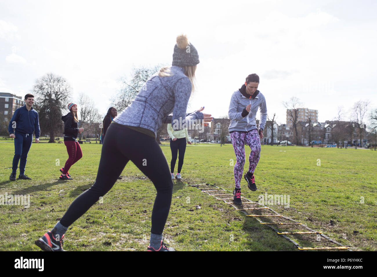 Woman cheering classmate doing speed ladder drill in sunny park Stock Photo