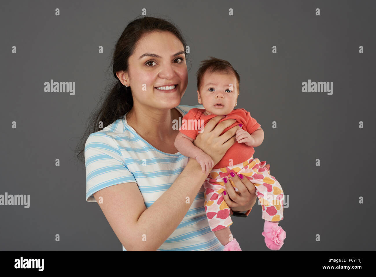 Young mom hold small baby girl isolated on grey background Stock Photo