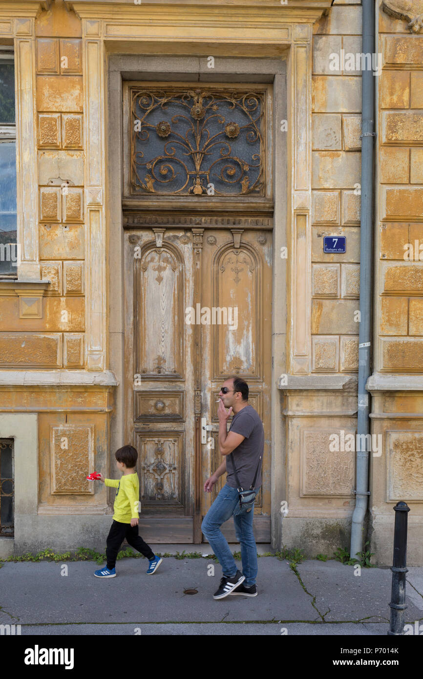 A smoking man and child walk past an old doorway and architecture, on 23rd June 2018, in Celje, Slovenia. Stock Photo