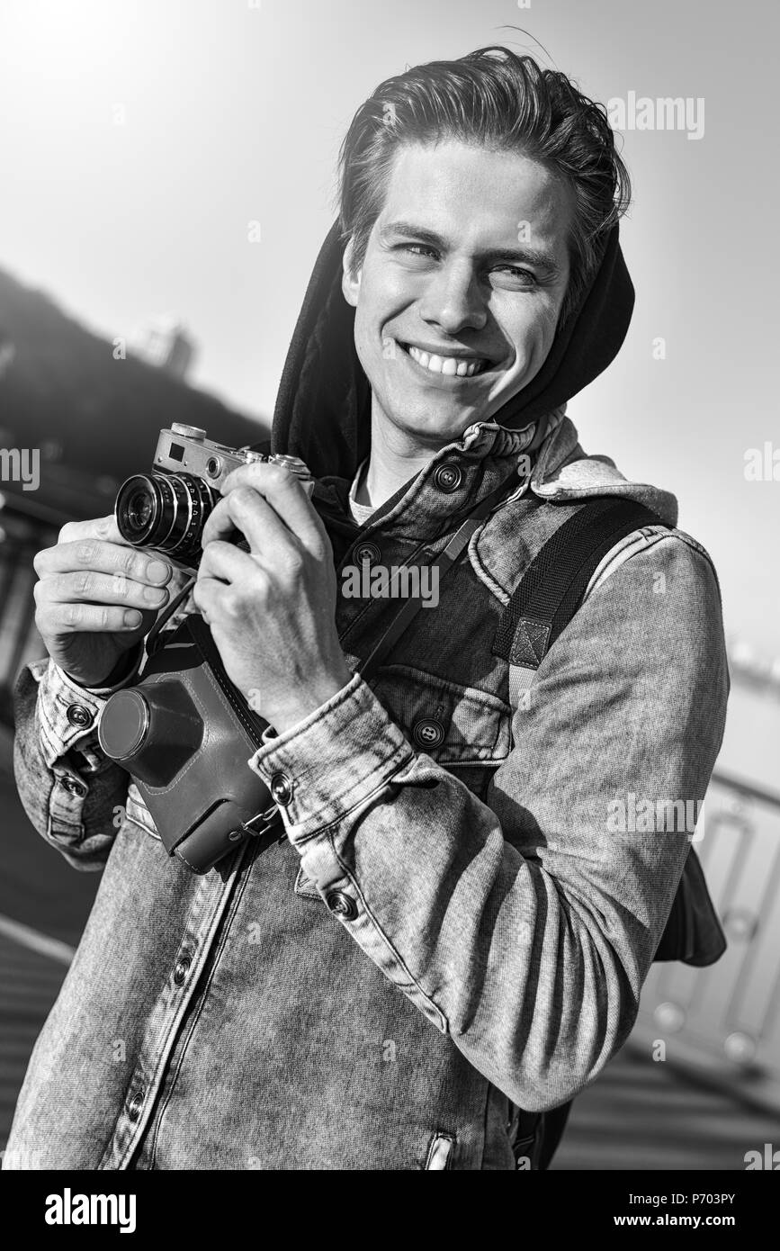 Stylish man photographing on retro camera. Tourist stay on the bridge and make a photo. Stock Photo