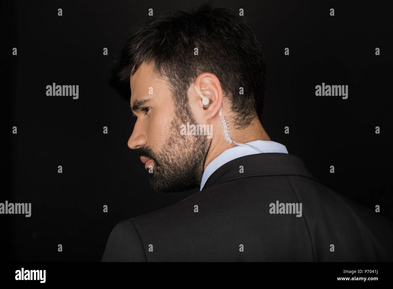 Secret service agent in suit using earphone, isolated on black Stock Photo