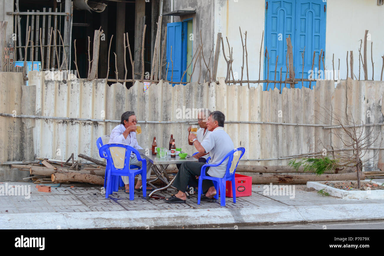 Phan Thiet, Vietnam - Mar 25, 2016. Local men drinking beer on street at sunset in Phan Thiet, Vietnam. Stock Photo