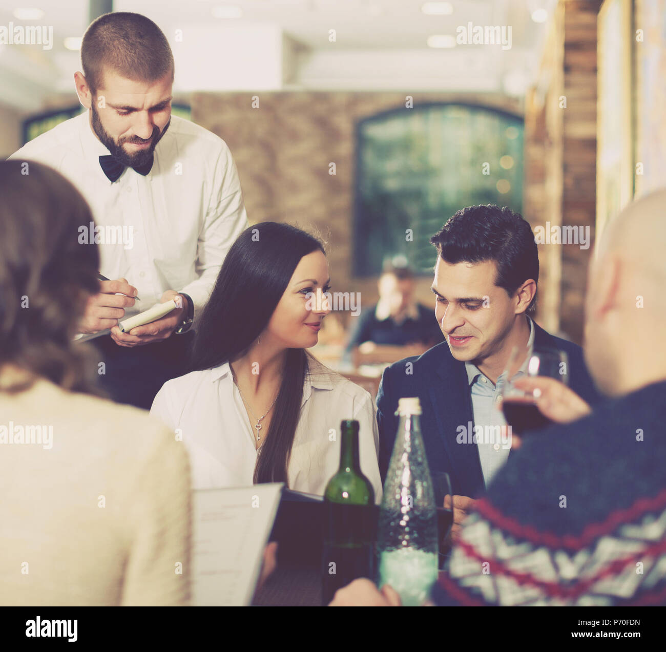 Employee positive adult waiter man taking order from positive guests at