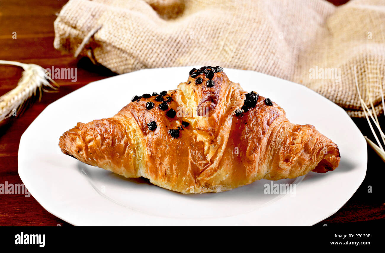 Delicious chocolate croissant with chocolate topping. Gourmet eating scene with wooden table and fresh butter croissant. Stock Photo