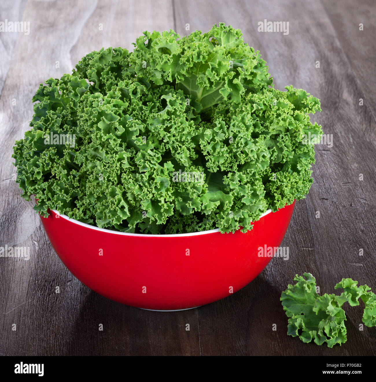 fresh green kale leaves in red ceramic bowl on vintage wooden table Stock Photo