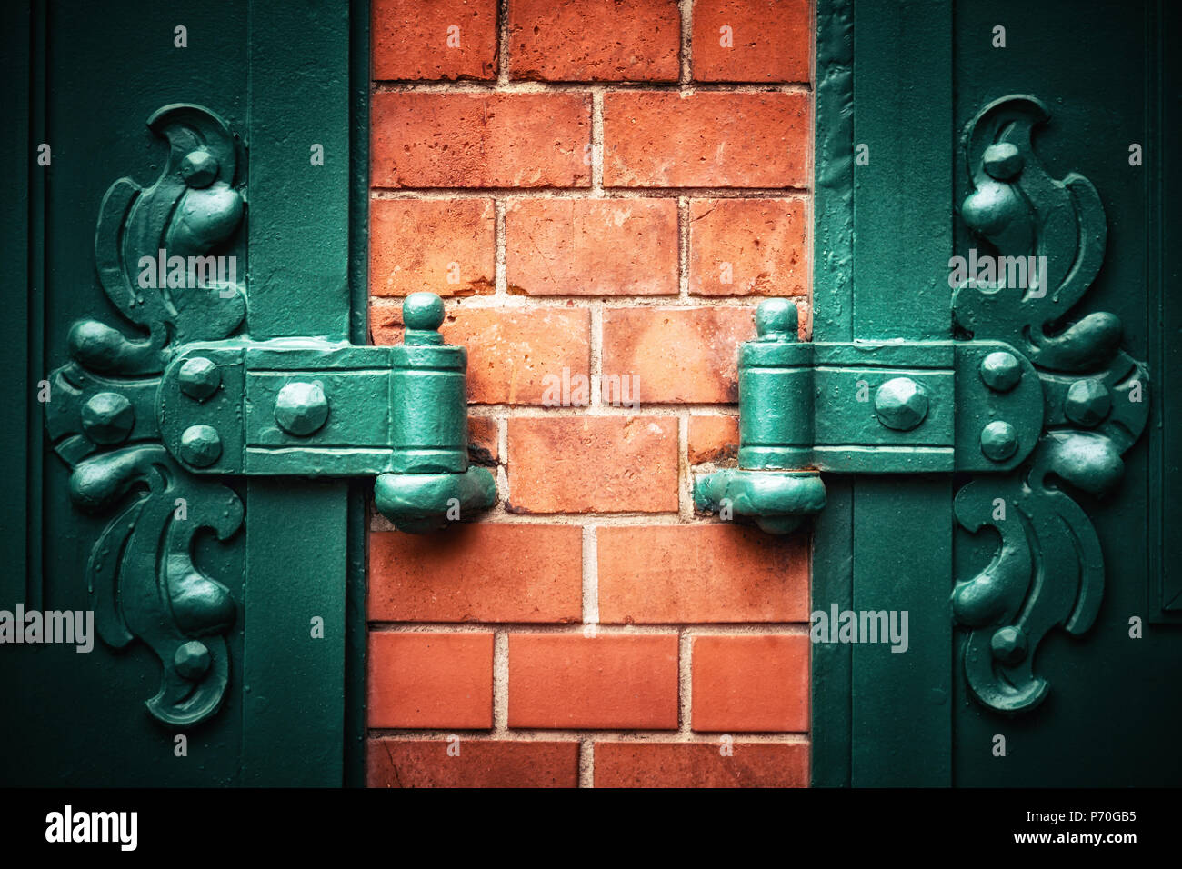 Symmetrical ornate metal hinges with red brick wall and vignette. Traditional style door detail in Berlin, Germany. Space for your text. Stock Photo