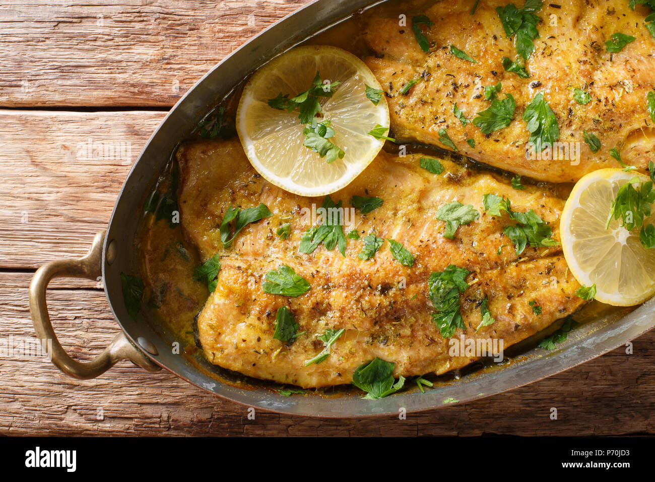Baked trout fish with garlic lemon butter sauce, parsley closeup in a copper frying pan on a