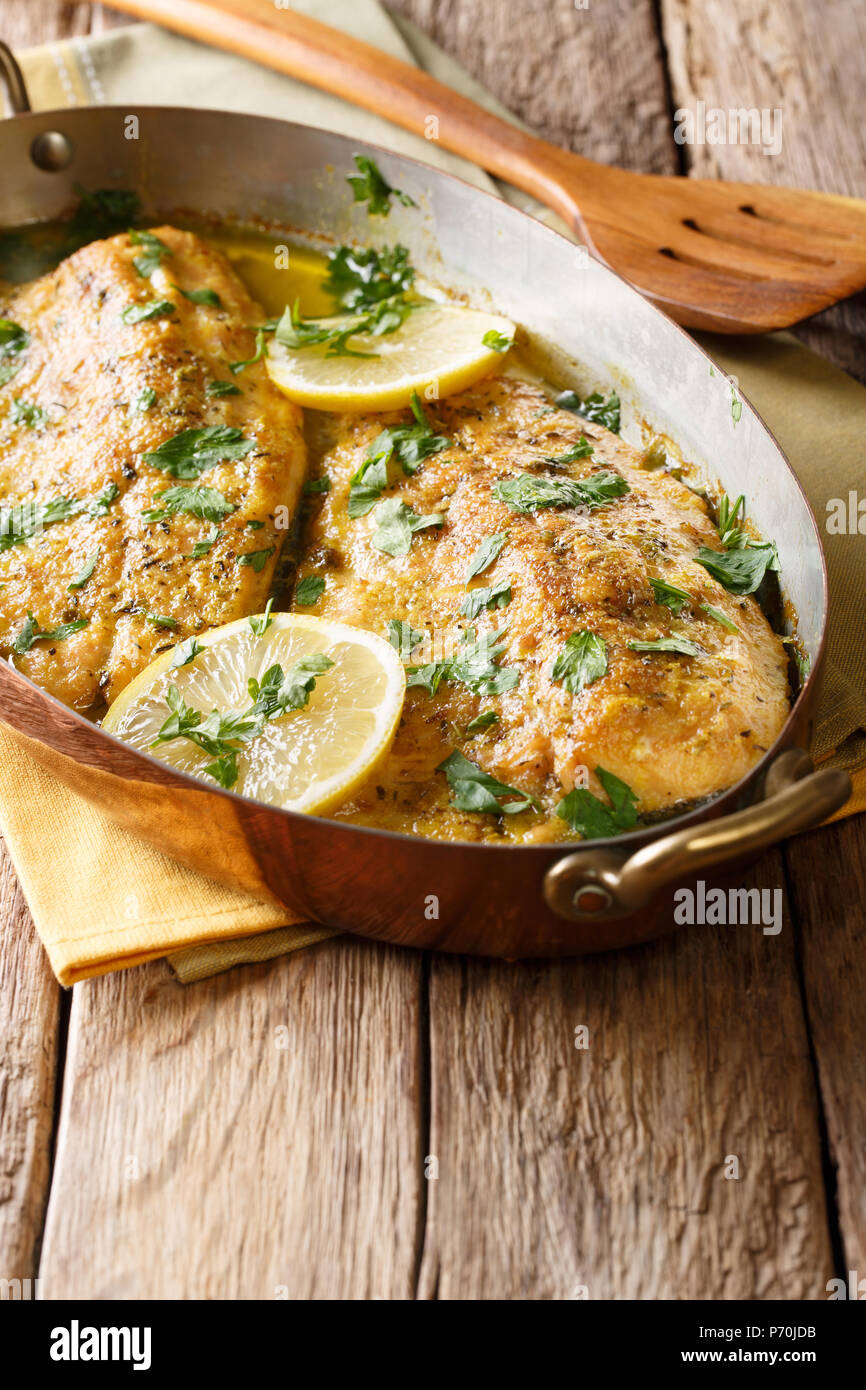 Traditional Mediterranean food: baked trout fillet with garlic butter sauce, lemon and parsley close-up in a copper frying pan on a table. vertical Stock Photo