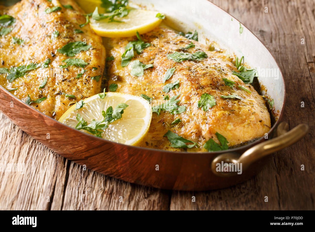 Baked trout fish with garlic lemon butter sauce, parsley closeup in a copper frying pan on a