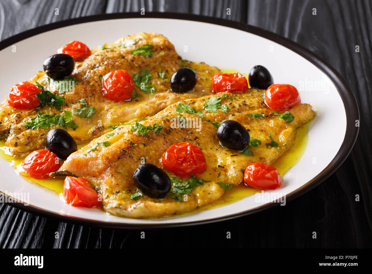 Mediterranean cuisine: fried trout fillets with garlic lemon butter sauce, tomatoes, parsley and olives close-up on a plate on a table. horizontal Stock Photo