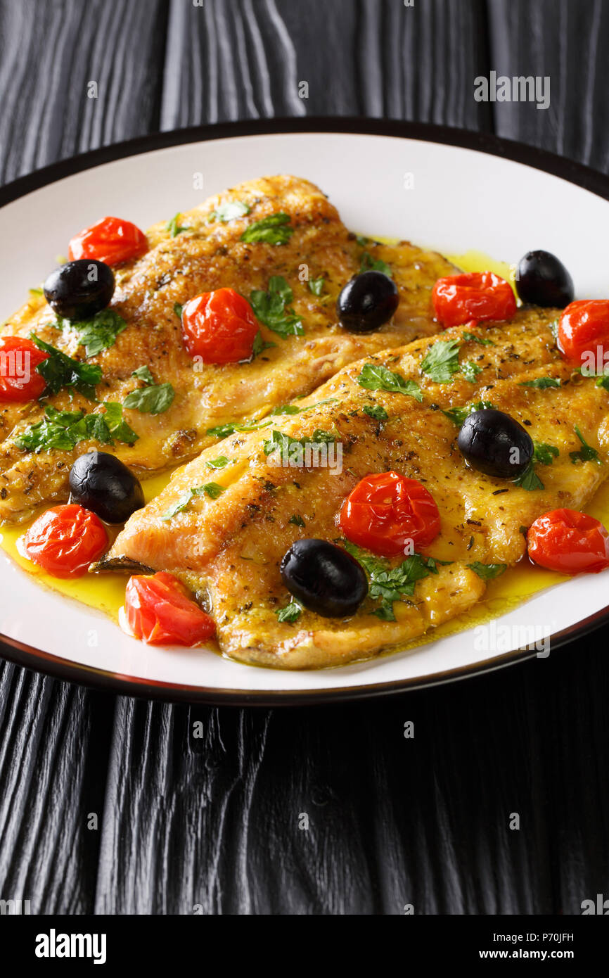 Spicy trout fillet with garlic lemon butter sauce, tomatoes and olives close-up on a plate on a table. vertical Stock Photo
