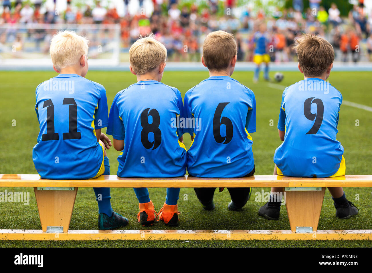 Football soccer tournament match for children. Kids substitute players sitting on a wooden bench. Football school competition for young boys Stock Photo