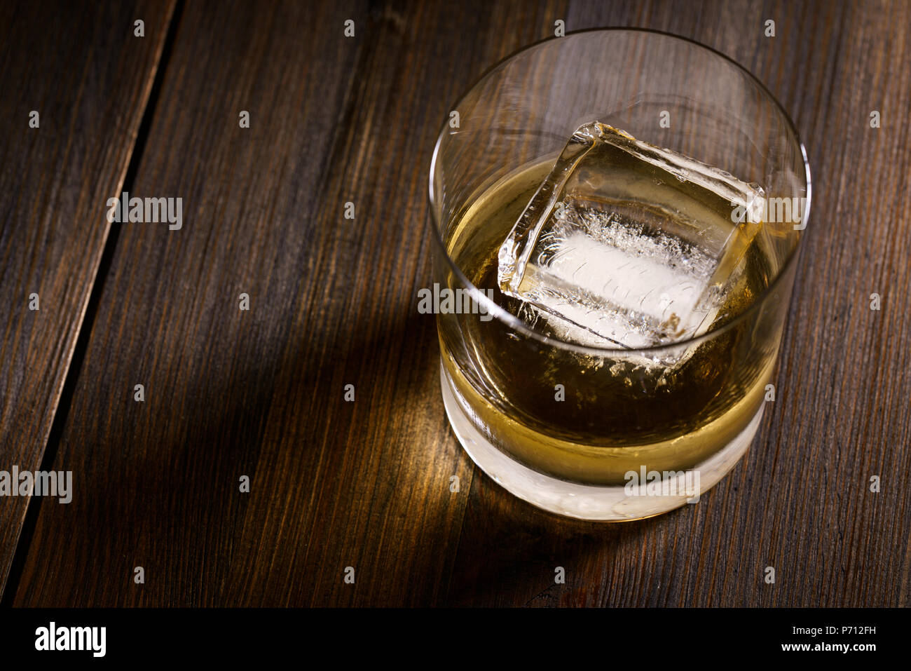 A glass of whisky with large ice cube. Dark wooden table, high resolution Stock Photo