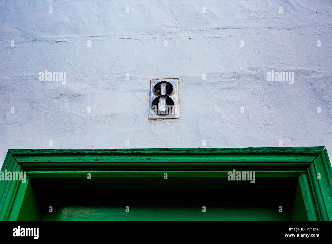 Ceramic black number eight, 8 outside on white painted wall over green wooden door Stock Photo
