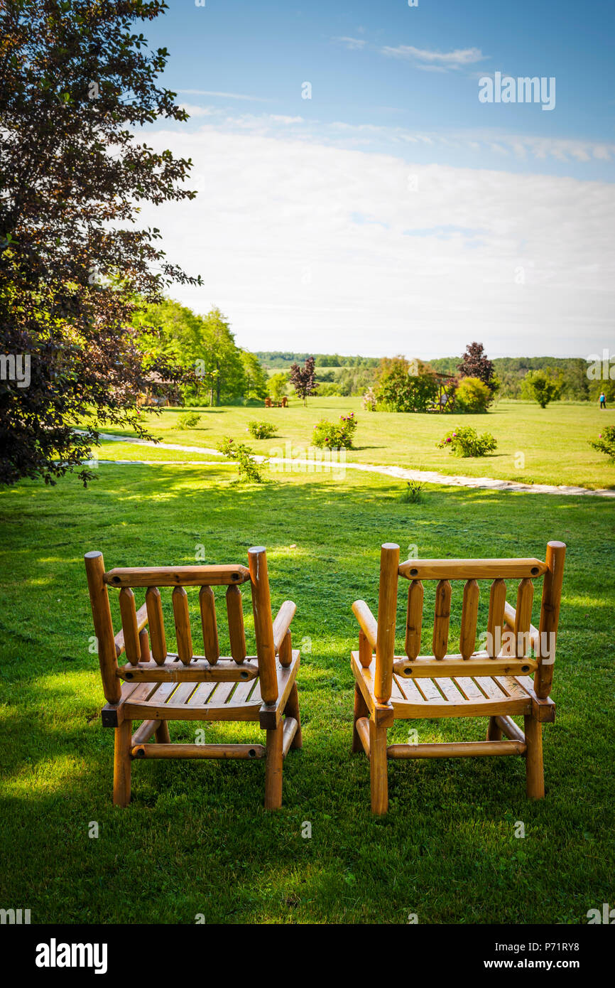 Two wooden chairs on lush green lawn with view of countryside in summer Stock Photo