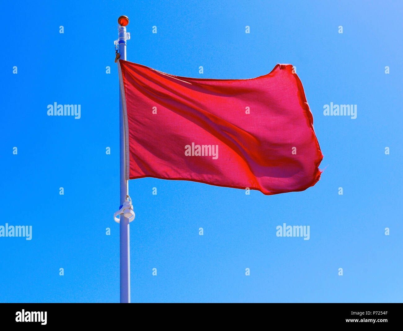 Red unsafe to bathe flag flying against blue sky Stock Photo