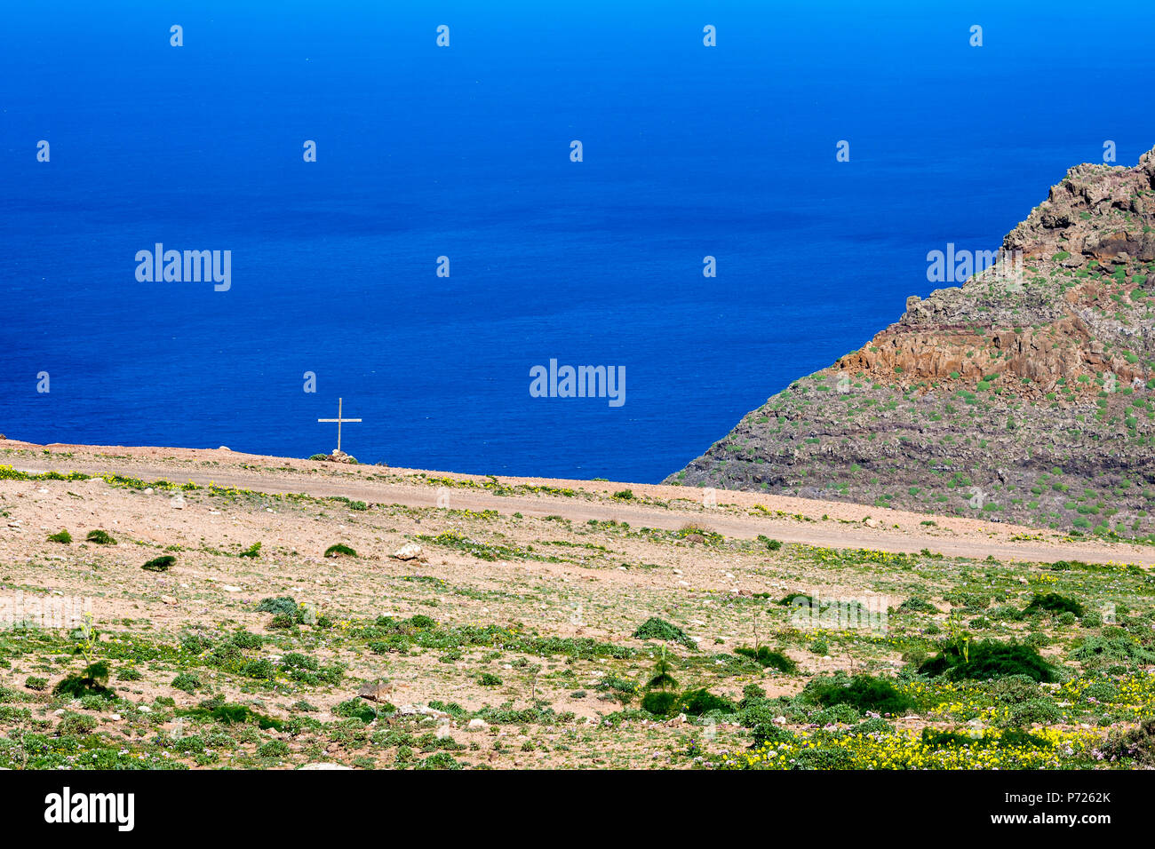 Lanzarote, Canary Islands, Spain, elevated landscape view of the blue Atlantic Ocean with Christian cross on a tomb near a dirt road close to the shore Stock Photo
