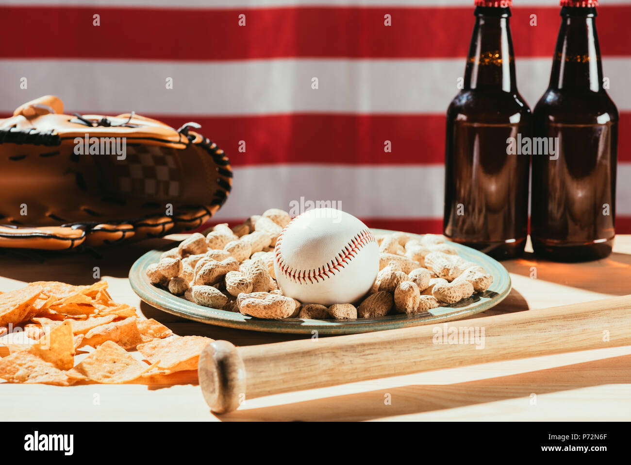 close-up view of baseball ball on plate with peanuts, bat and beer bottles, leather glove and american flag Stock Photo