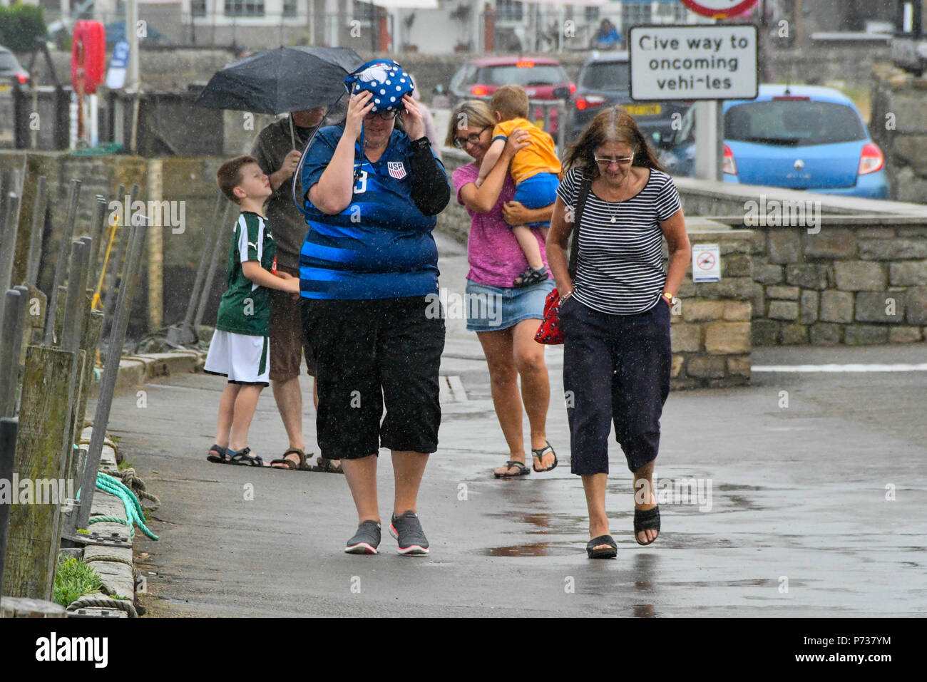 West Bay, Dorset, UK.  4th July 2018. UK Weather.  Visitors next to the harbour at the seaside resort of West Bay in Dorset try their best to stay dry as rain falls from a shower.  Picture Credit: Graham Hunt/Alamy Live News Stock Photo
