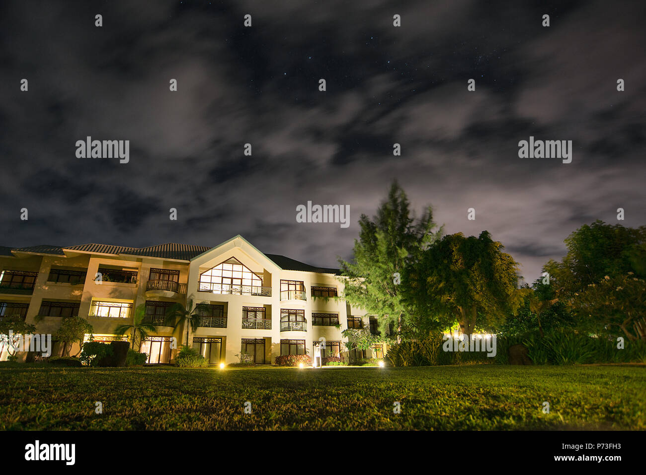 Wide angle ground level shot of a hotel in Mauritius at night with moving clouds, lights, trees, lawn Stock Photo
