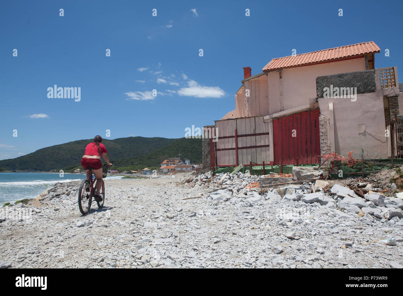 Florianopolis, Santa Catarina, Brazil. Girl riding a bike on a street destroyed by the waves of the sea. Effect of rising sea level. Stock Photo