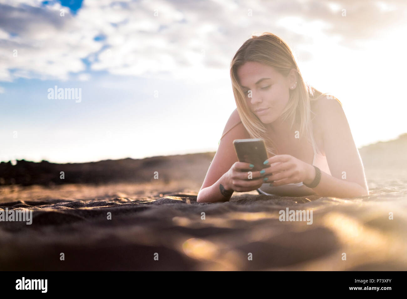 young beautiful blonde woman lay down at the beach in vacation and lifestyle leisure activity using a smartphone to check social media and use interne Stock Photo