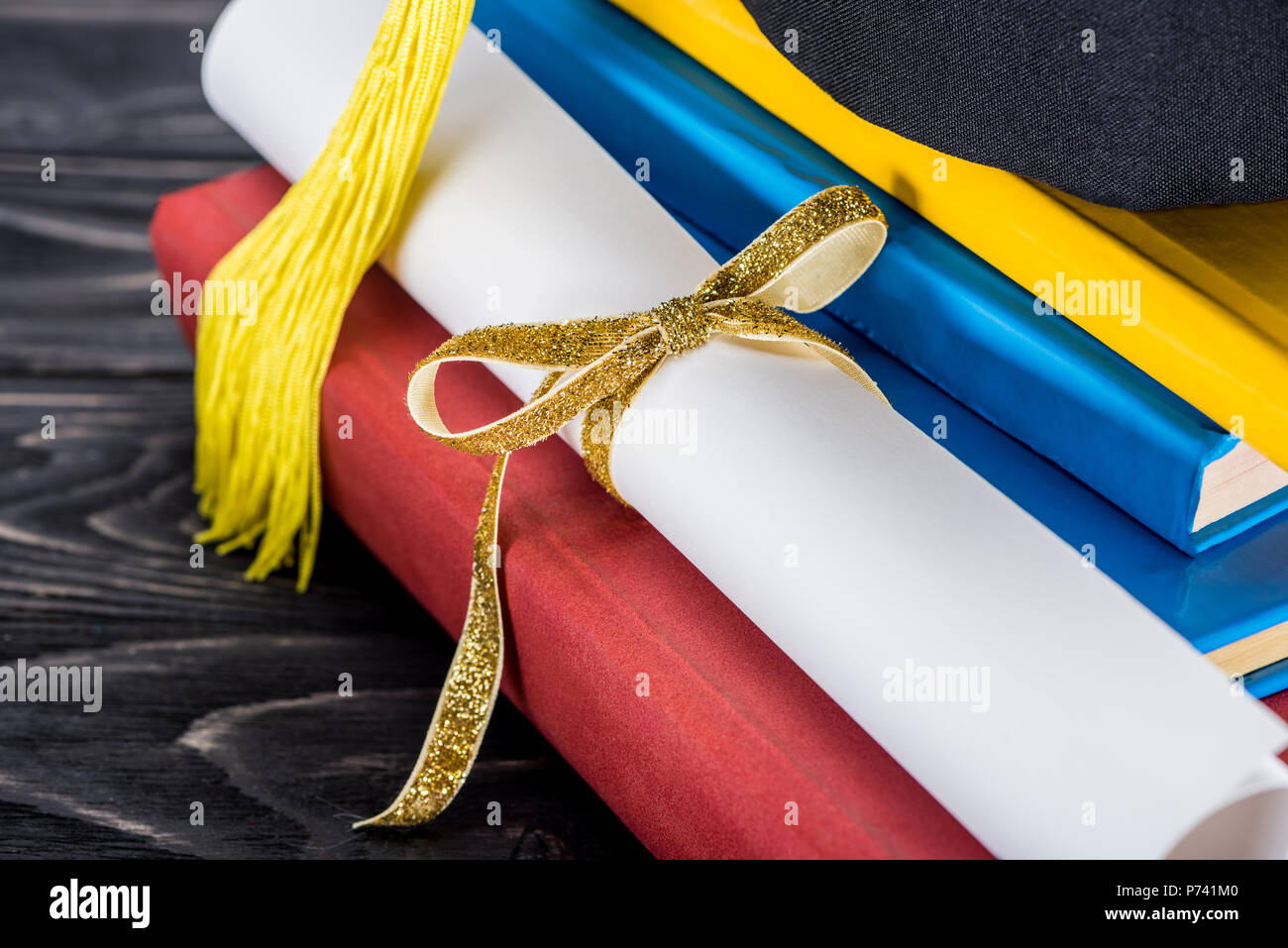 Graduation hat and diploma with yellow ribbon on stack of books Stock ...