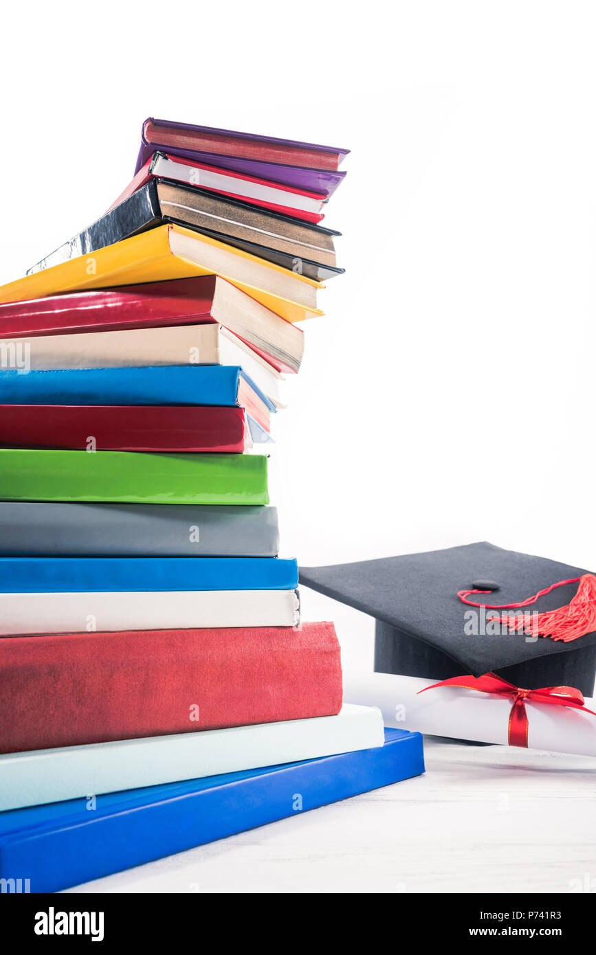 Graduation hat and diploma with red ribbon by books on table Stock ...