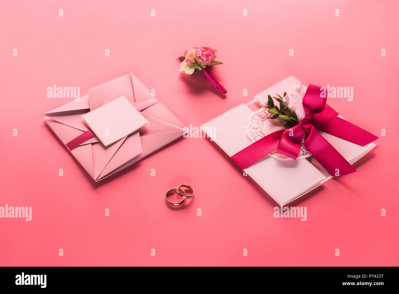 wedding rings, boutonniere and pink envelopes with invitations on pink surface Stock Photo