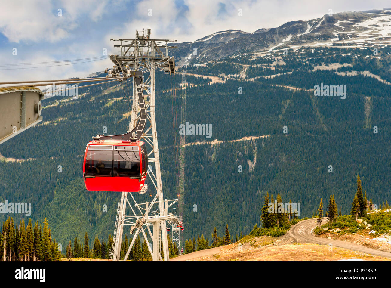 Top view of thick, fluffy white clouds in the blue sky over wooded mountains with dirt road, country road, coniferous trees, cable car with red gondol Stock Photo