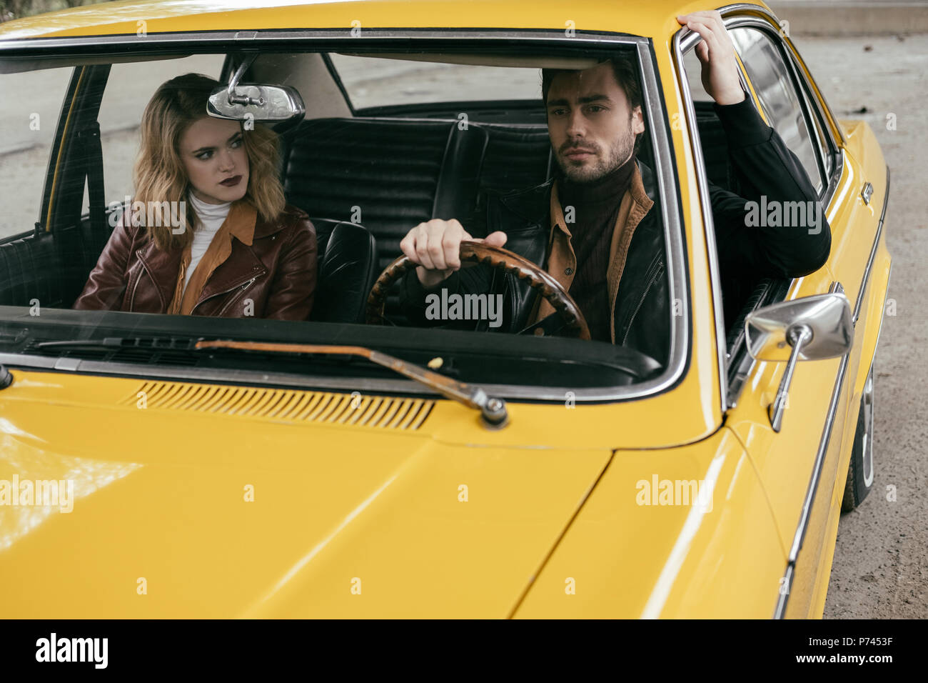 view through the windshield of young couple in leather jackets sitting together in yellow classic car Stock Photo