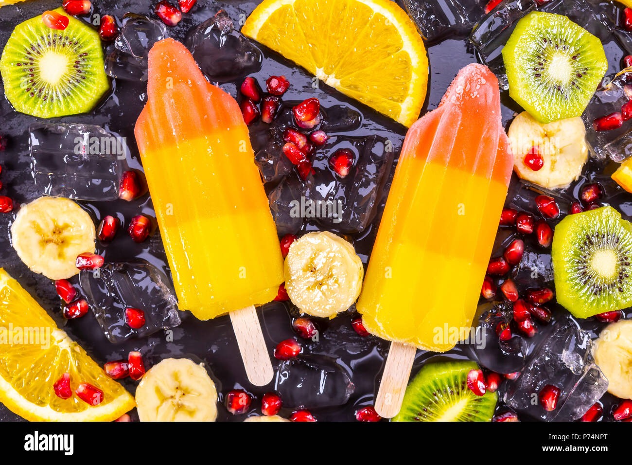 Fruit ice cream on stick with slices fruits on black slate board. Focus on Popsicles. Stock Photo