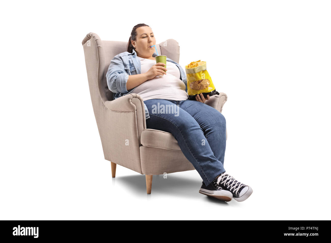 Overweight woman with a drink and a bag of chips sitting in an armchair isolated on white background Stock Photo