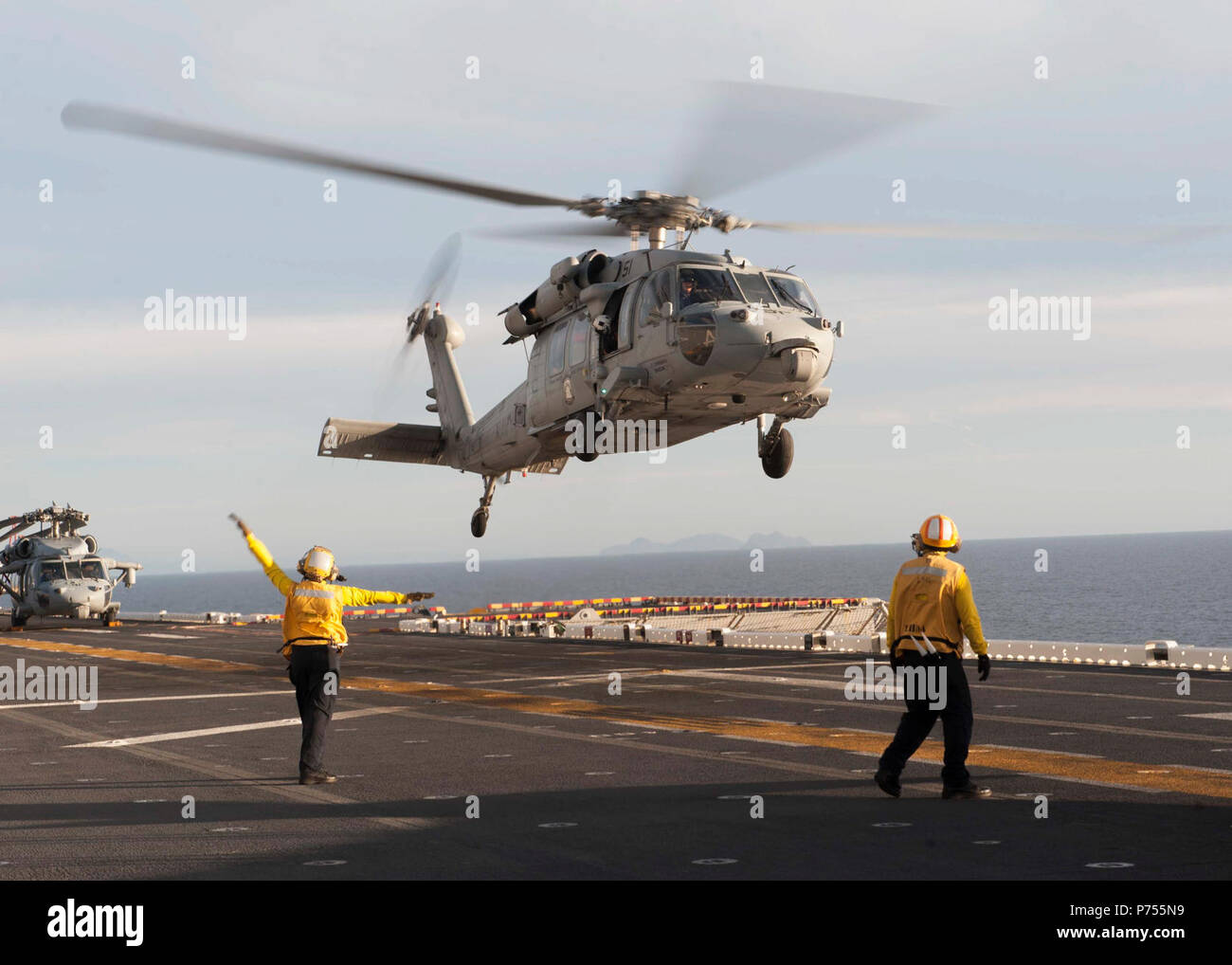 OCEAN (Dec. 3, 2015) An aviation boatswain’s mate (handling) signals to the pilot of an MH-60S Sea Hawk helicopter assigned to the “Wild Cards” of Helicopter Sea Combat Squadron (HSC) 23 on the flight deck of the amphibious assault ship USS Boxer (LHD 4). The Boxer Amphibious Ready Group (ARG) is underway off the coast of Southern California completing a certification exercise (CERTEX). CERTEX is the final evaluation of the 13th Marine Expeditionary Unit (13th MEU) and Boxer ARG prior to deployment and is intended to certify their readiness to conduct integrated missions across the full spectr Stock Photo