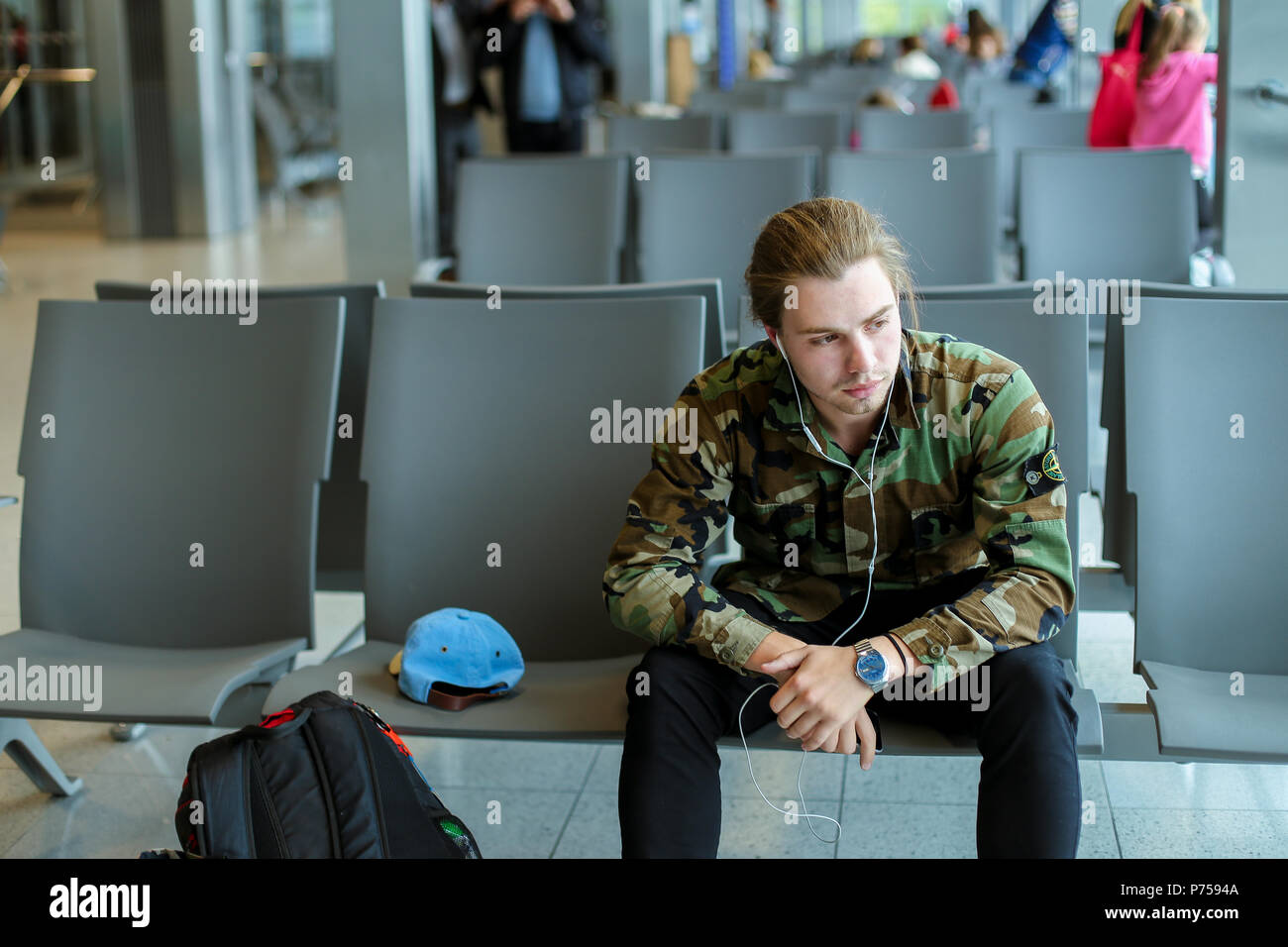 Caucasian male student sitting in waiting room at airport and listening to music. Stock Photo