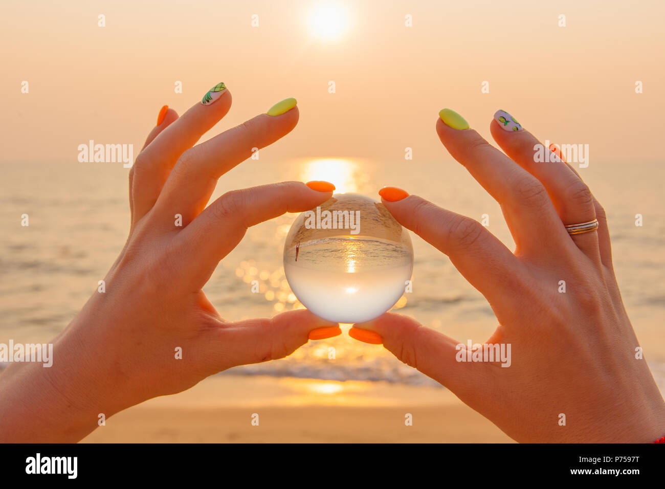 Crystal lens ball in hand with reflection of sea and sunset on the ...