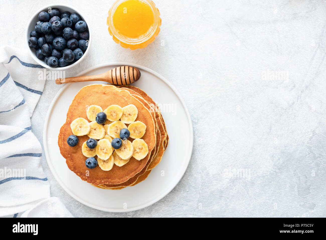 Buttermilk Pancakes with banana, blueberries and honey on concrete background. Top view and copy space for text. Top view of pancakes with berries on  Stock Photo