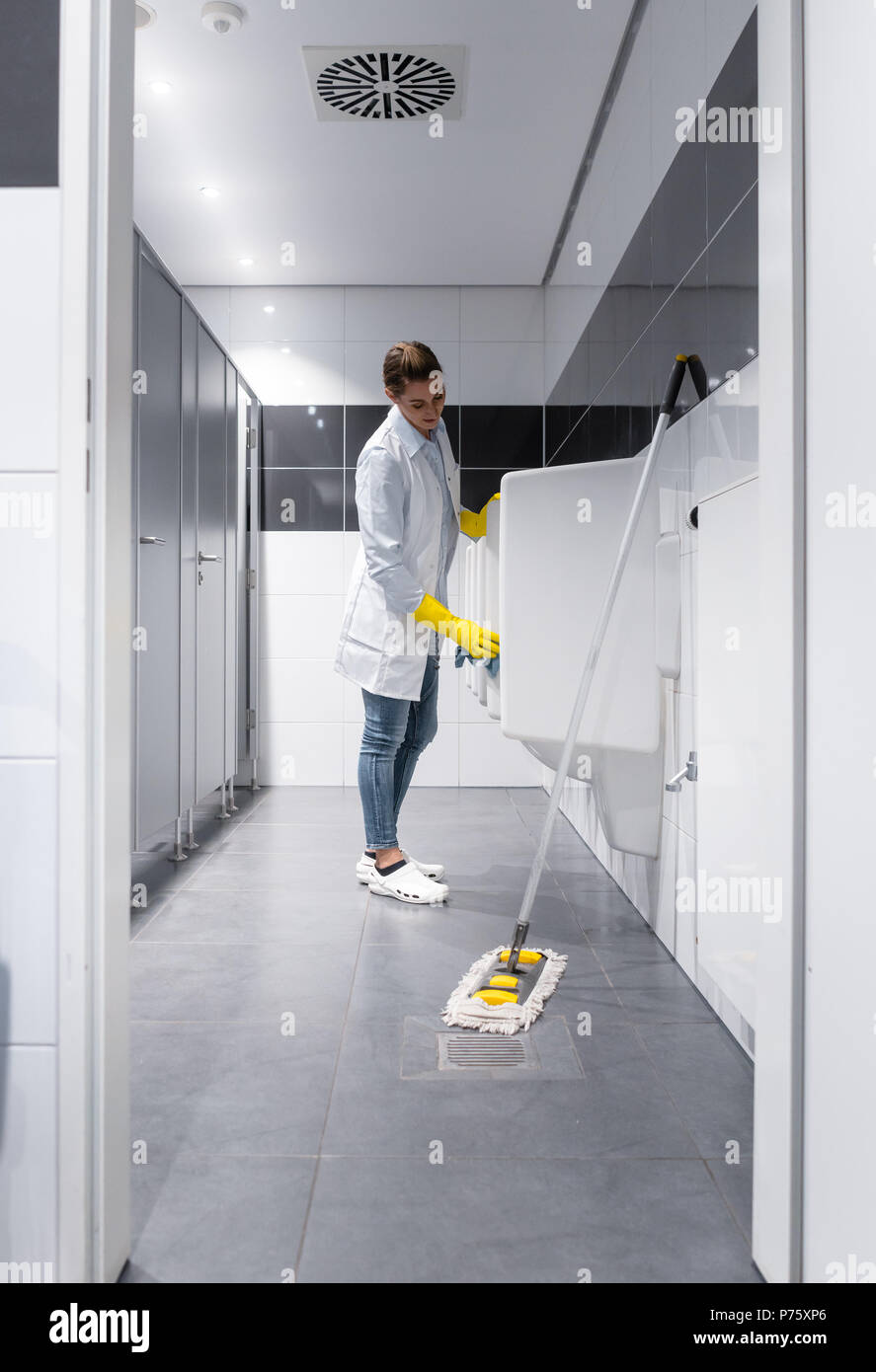 Janitor woman cleaning urinals in public toilet  Stock Photo