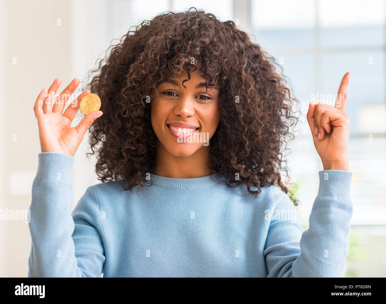 African american woman holding golden bitcoin cryptocurrency at home  surprised with an idea or question pointing finger with happy face, number  one Stock Photo - Alamy