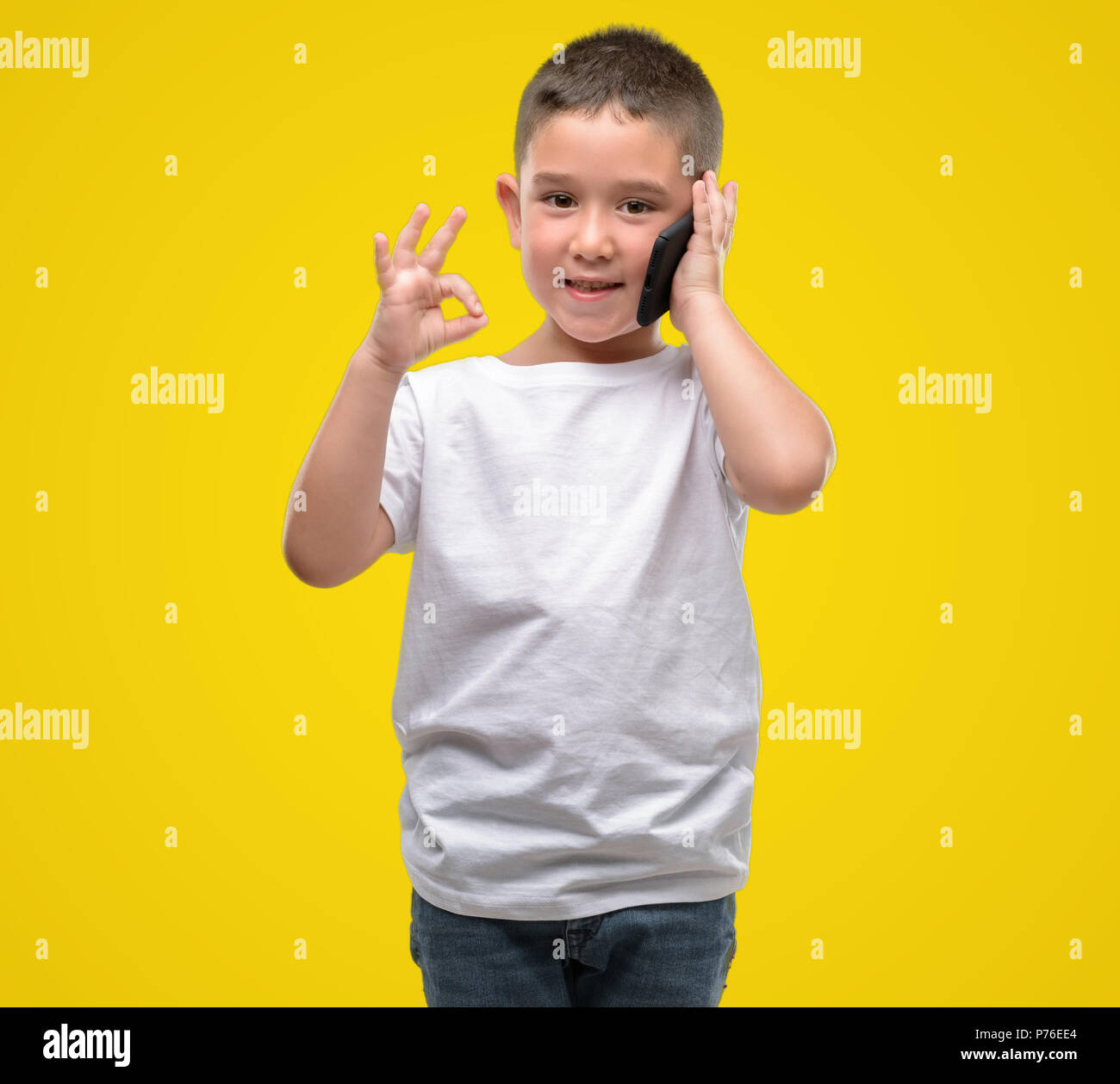 Dark haired little child using a smartphone doing ok sign with fingers ...
