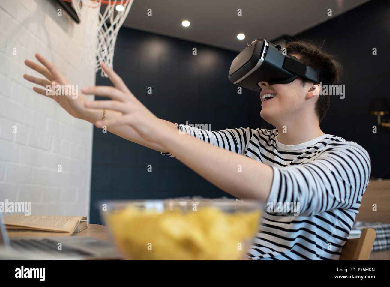 Excited young male extending hands forward while using virtual reality headset sitting at home. Stock Photo