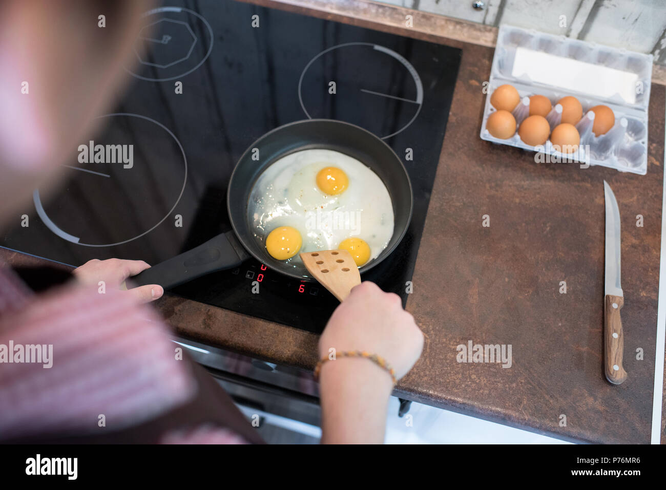 Anonymous young man standing in kitchen and preparing eggs for breakfast while spending time alone. Stock Photo